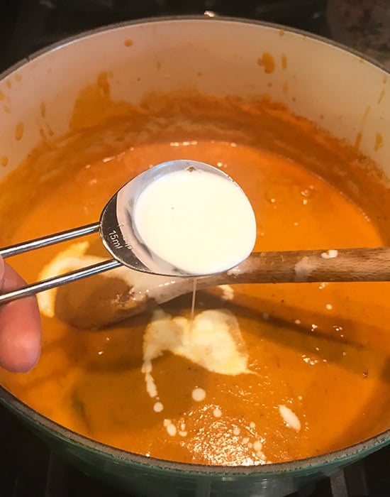 spoonful of cream is being added to a curry