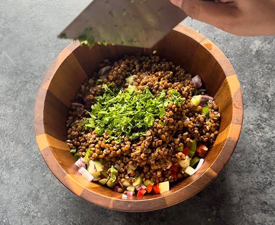a hand adding fresh herbs to a salad bowl using a bench scraper