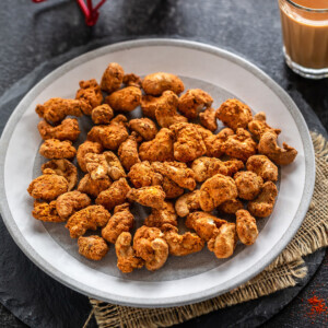 spice coated cashews on a plate with glass of chai on the side and also in the back