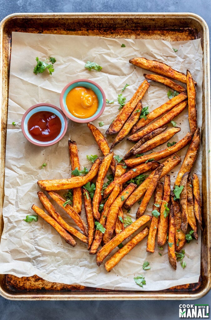 french fries coated with spices placed on a baking tray with 2 bowls of dipping sauces
