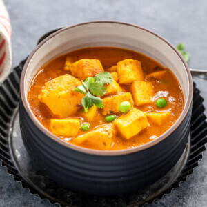 curry of potatoes, paneer and peas served in a black bowl and garnished with cilantro