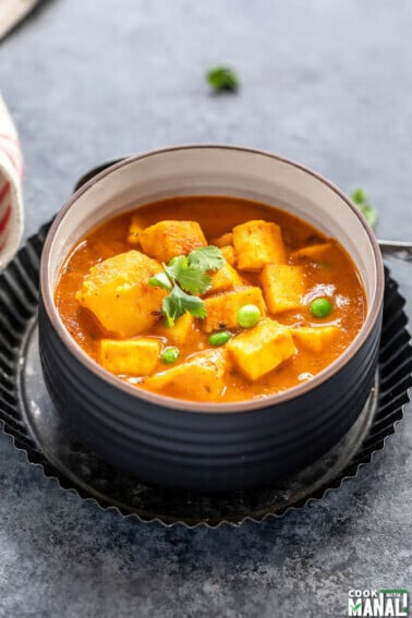 curry of potatoes, paneer and peas served in a black bowl and garnished with cilantro