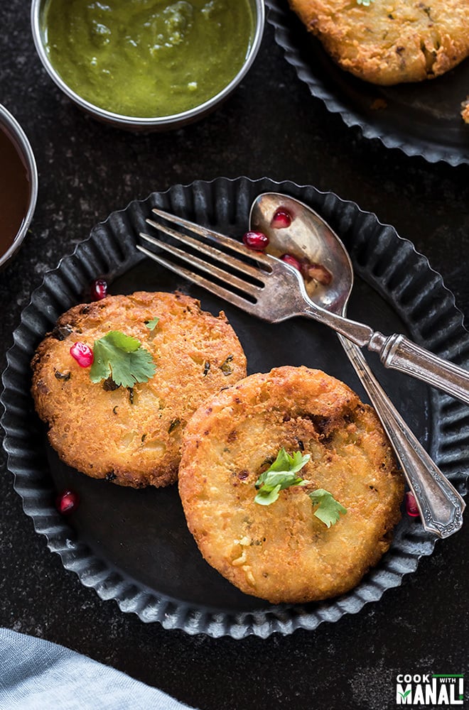 two pieces of aloo tikki in a rimmed plate along with a spoon and fork