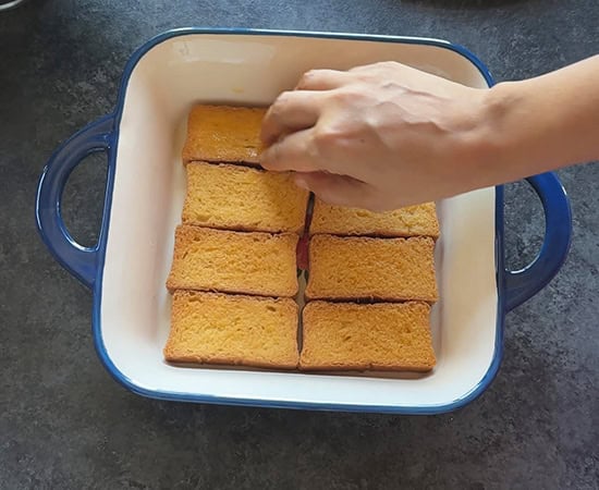 a hand layering rusks in a pan