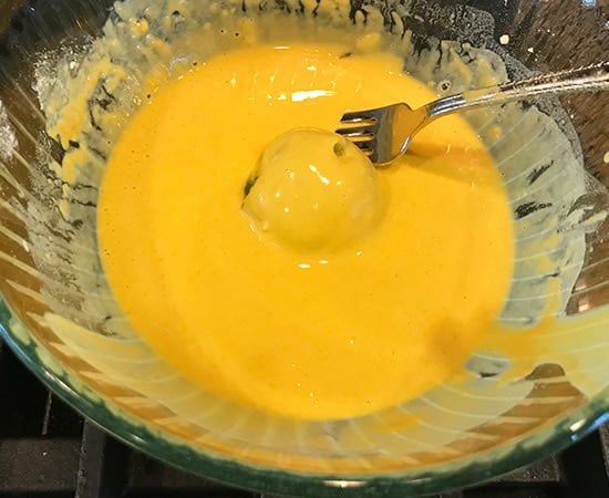 potato ball being dipped in besan batter using a fork