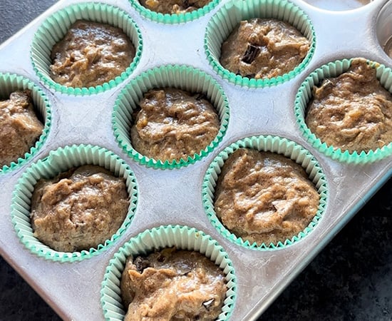 muffin tin with cupcake liners which are filled with muffin batter