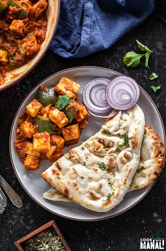 kadai paneer served with naan and onion rings in a white plate