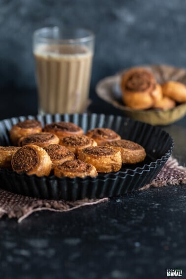 bhakarwadhi placed in a black plate with glass of chai in the background