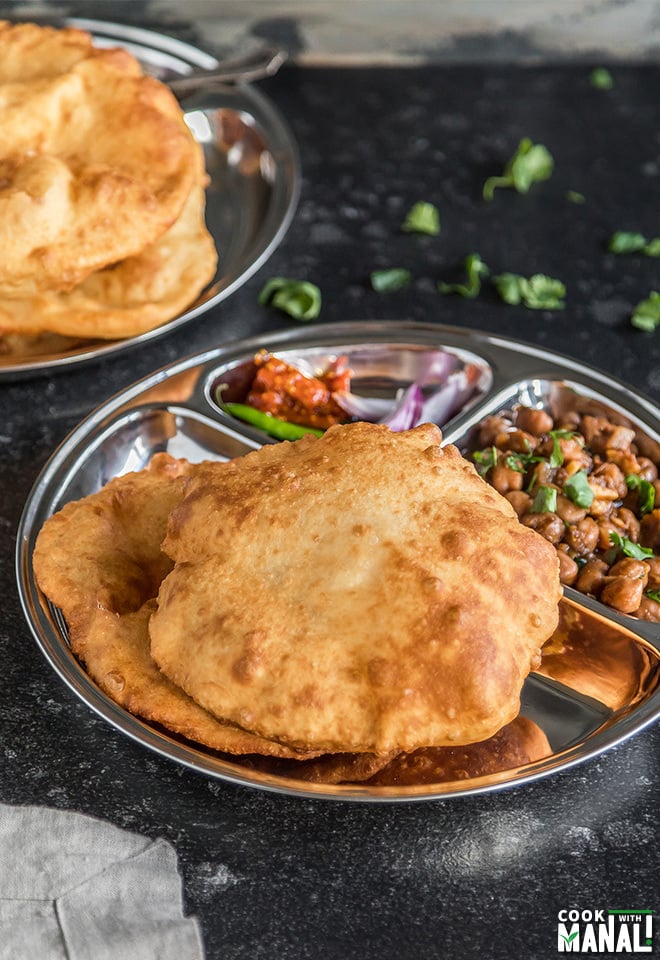chole bhatura in a round steel plate with onions and pickle