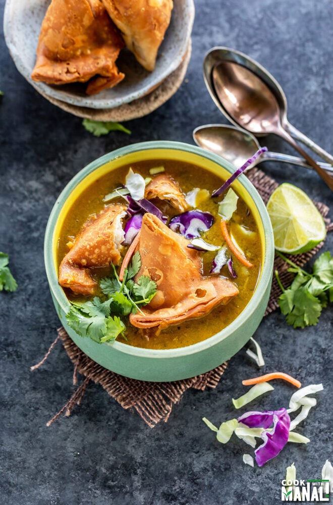 soup bowl topped with samosa, cilantro, sliced cabbage with lime wedge on the side