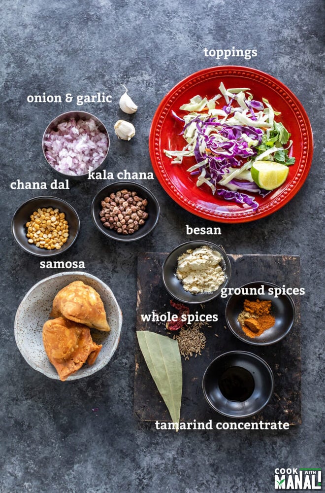 several bowls filled with spices, lentils, samosa etc, placed on a board