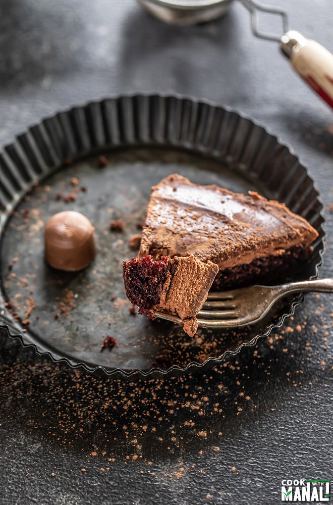 fork cutting a chocolate cake placed in a rimmed grey plate