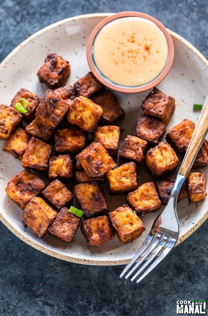 crispy tofu served in a white plate with a small bowl of dipping sauce