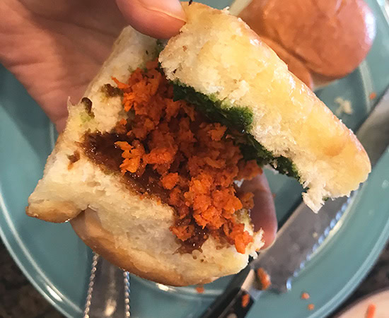 a dinner rolls being split in half to show the chutney smeared on the inside