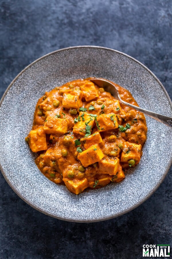 matar paneer served in a bowl with spoon on the side