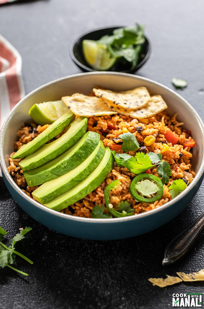 bowl of rice, beans topped with avocado slices, jalapeño, tortilla chips with a napkin placed on the side