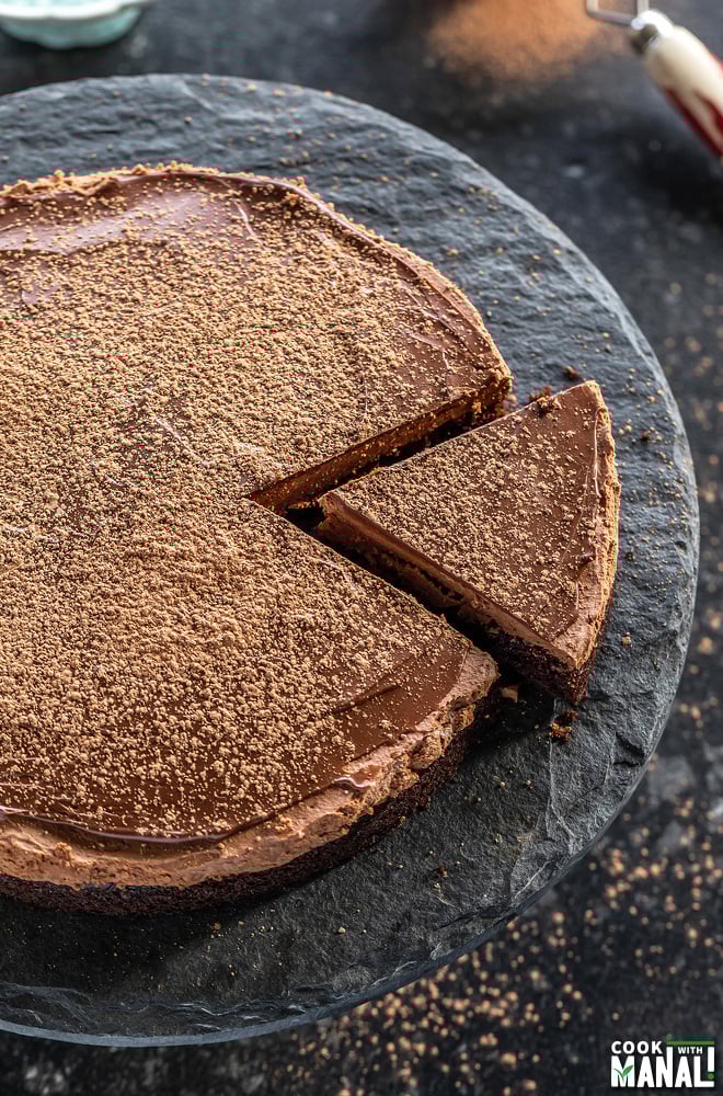 a slice of chocolate cake being cut from the cake placed on a black color cake stand