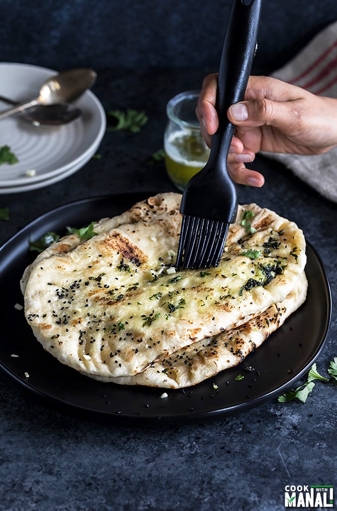 garlic naan being brushed with butter with a black pastry brush