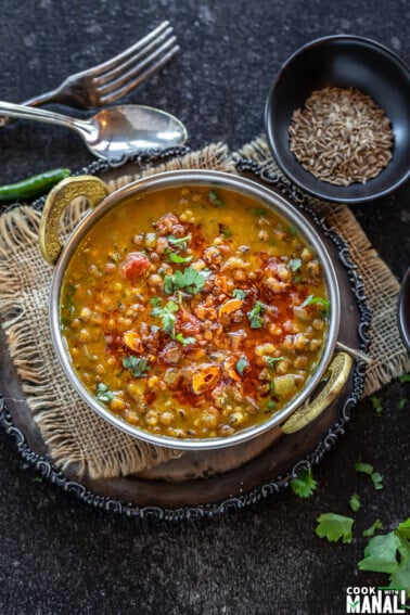 green lentils served in a copper kadai and garnished with cilantro and spices