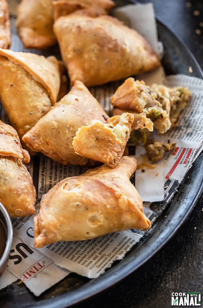 plate of samosas with one samosa broken to show the interior potato filling and the flaky crust