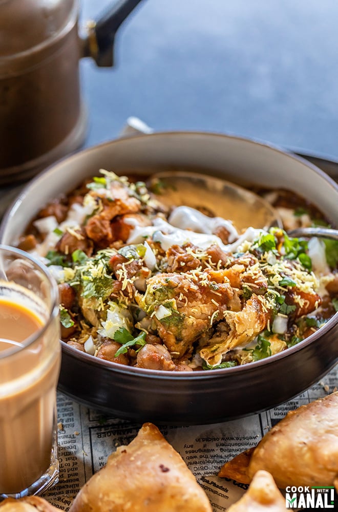 bowl of samosa chaat with broken samosa placed in the side and a cup of chai kept on one side of the bowl