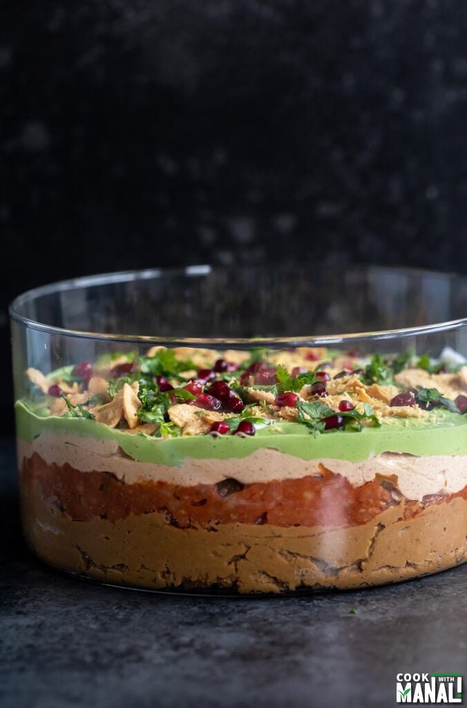 layered dip served in a transparent bowl topped with cilantro, pomegranate