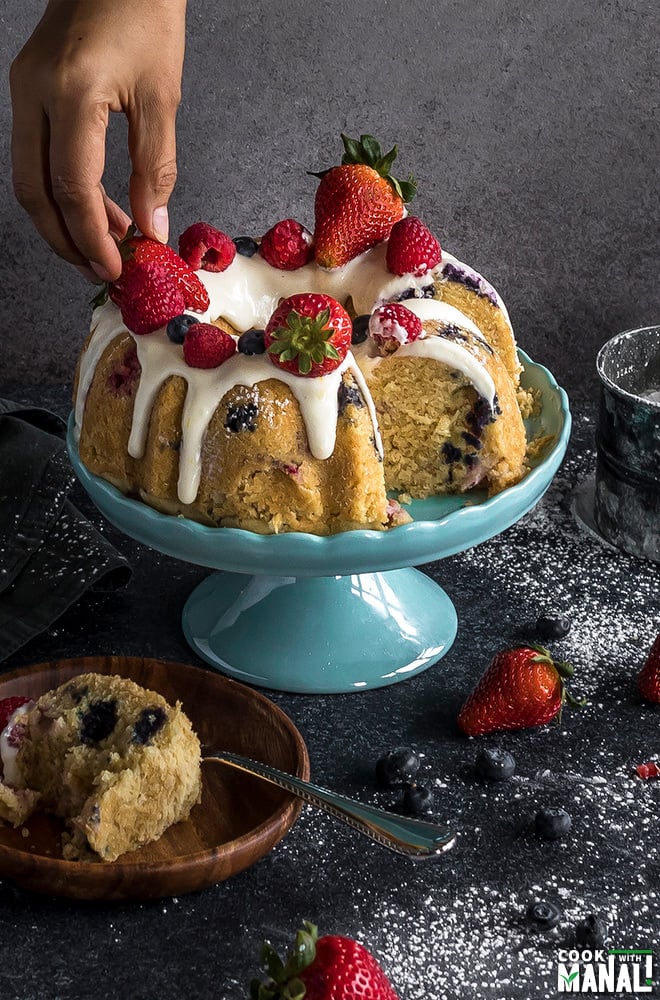 a hand placing a strawberry on a bundt cake placed on a blue cake stand
