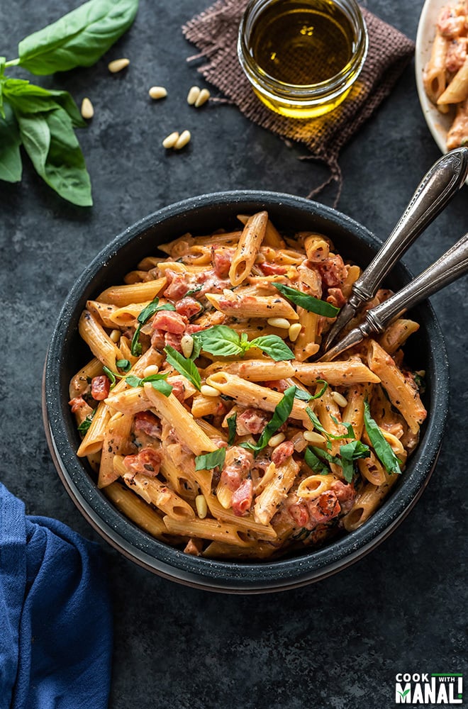 tomato basil pasta in a black bowl with 2 forks. There are also some basil leaves and a small jar of olive oil in the background