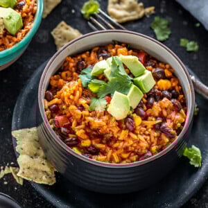 enchilada rice in a black bowl topped with avocados with a side of tortilla chips