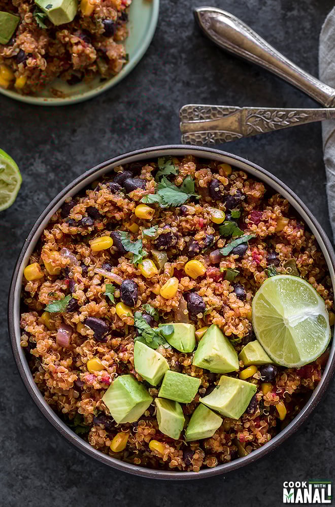 mexican quinoa in a round black bowl, garnished with diced avocados and a lime wedge