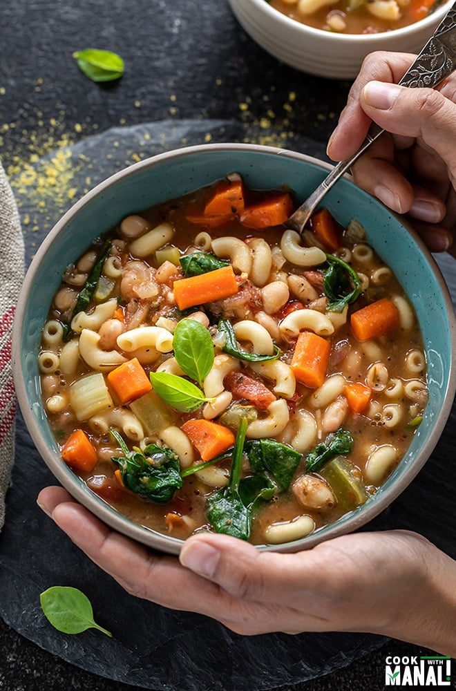 pair of hands holding a soup into a bowl of minestrone soup