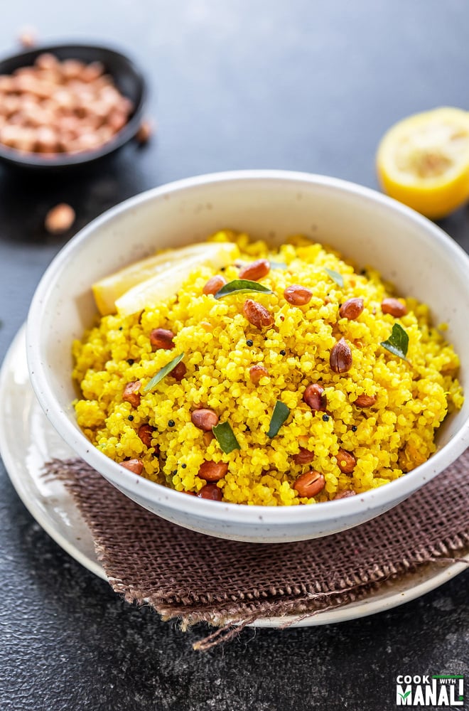 white bowl with yellow color quinoa topped with peanuts, with a wedge of lemon in the background along with a bowl of peanuts