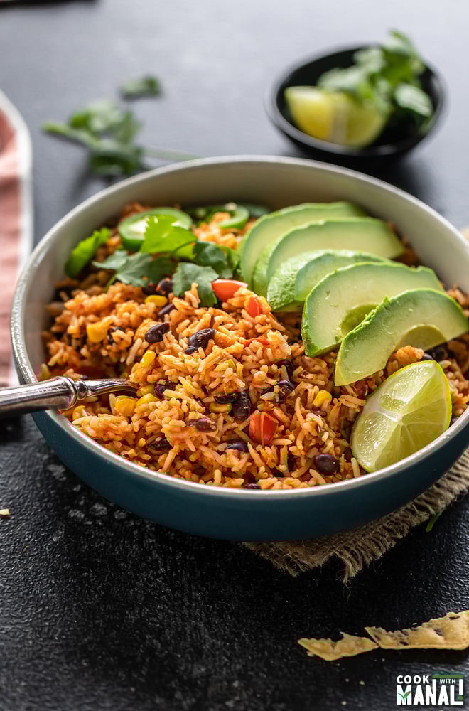 vegan burrito bowl filled with rice beans, served with a fork and topped with avocado slices, cilantro, lime wedge and jalapeño