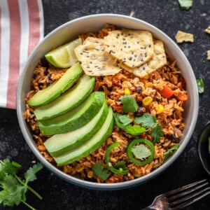 bowl filled with rice, beans and topped with avocado slices, tortilla chips, cilantro and jalapeño