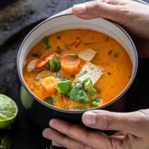 pair of hands holding a bowl of thai curry soup