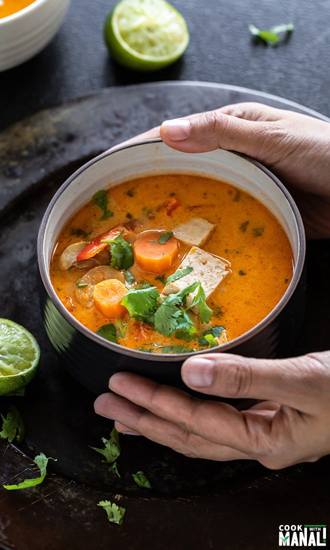pair of hands holding a bowl of thai curry soup