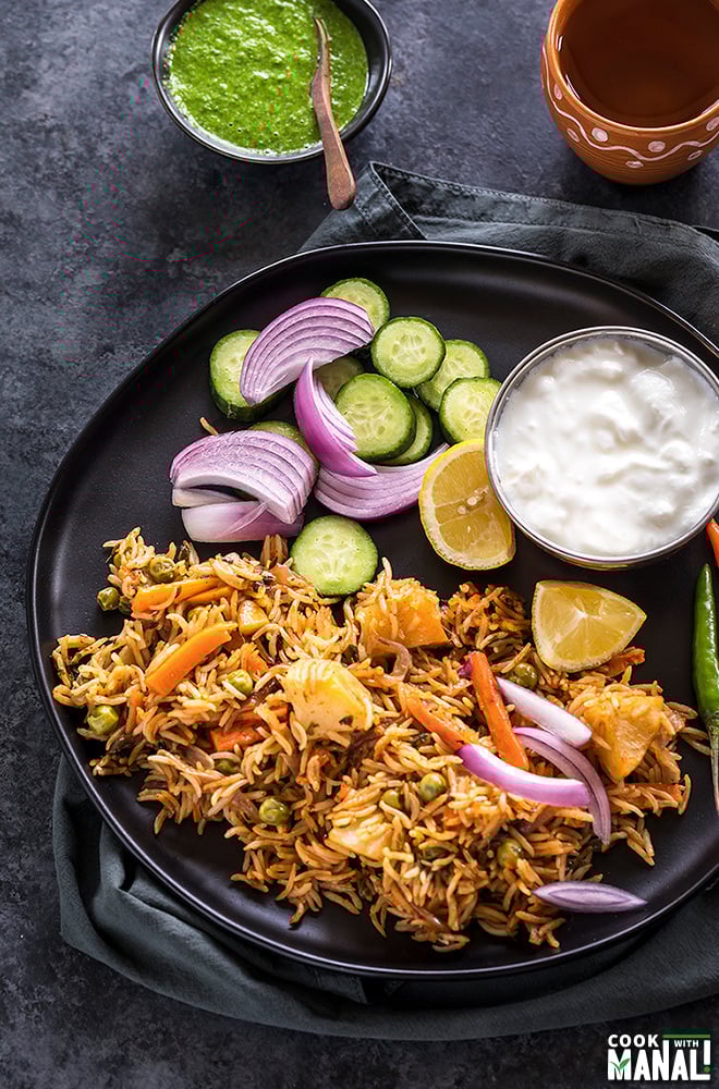 instant pot vegetable biryani in a black plate with sliced onion and lemons and bowl of yogurt