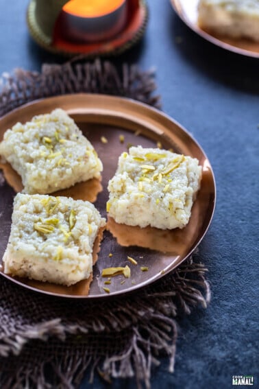 3 pieces of kalakand served on a small round copper plate with a tealight in the background