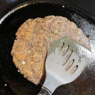 spatula pressing a buckwheat flour flatbread being cooked on a skillet