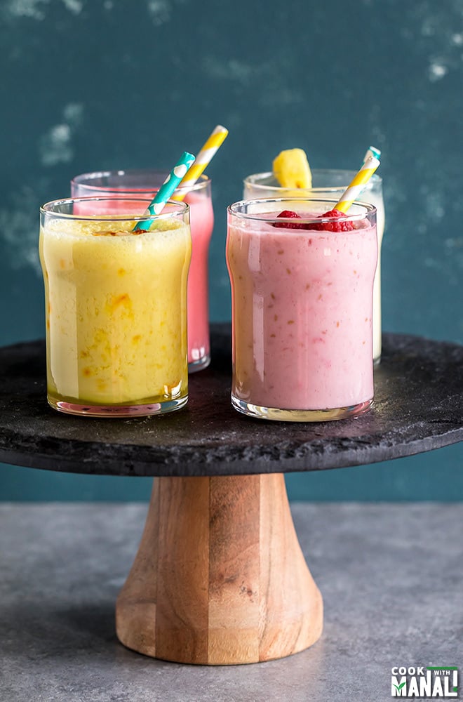 four glasses of lassi with straw on a cake stand
