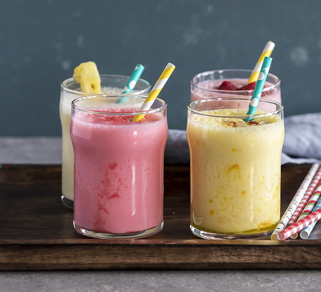 four glasses of lassi with straws in a wooden tray