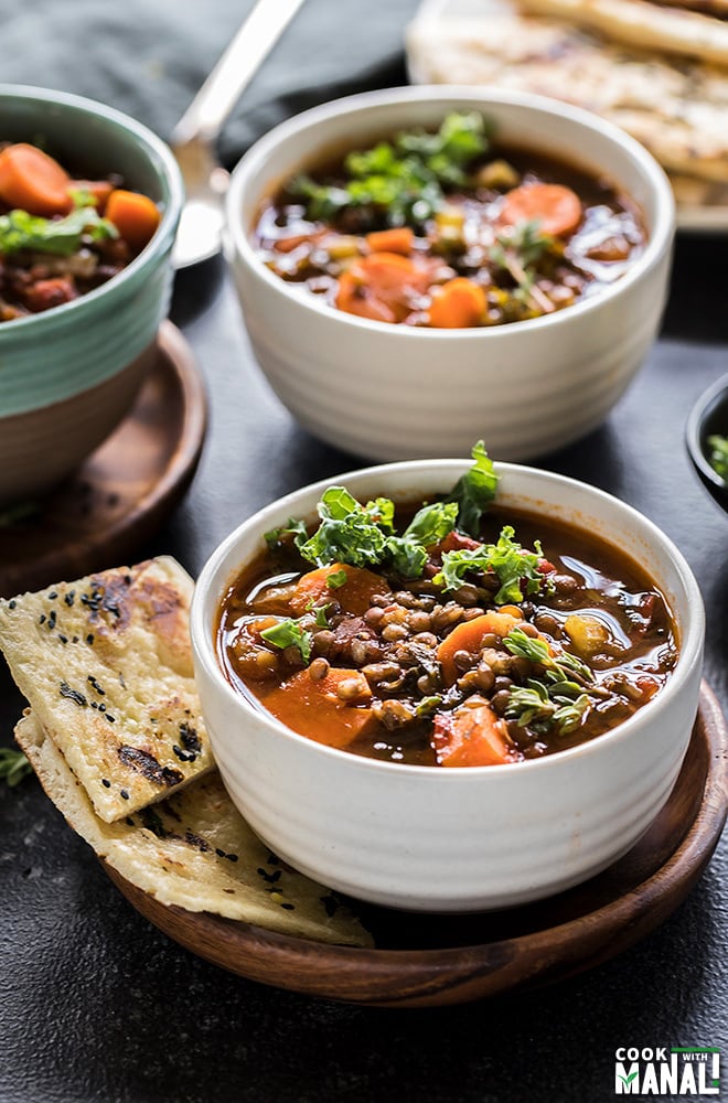 vegan lentil soup in a white bowl with bread on the side and more bowls of lentil soup on the side and back