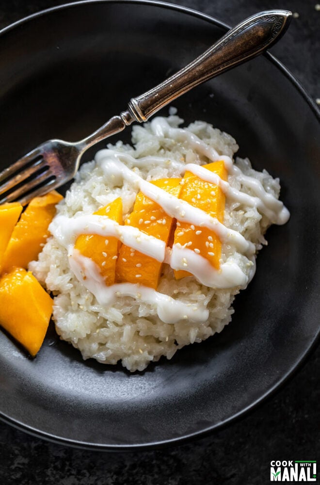 sticky rice drizzled with coconut sauce and topped with sesame seeds served with slices of mangoes