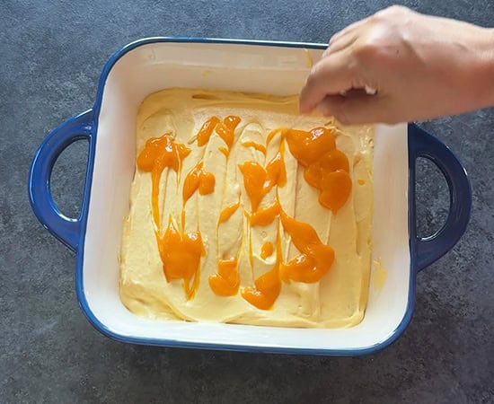 a hand making swirling design on top of mango tiramisu