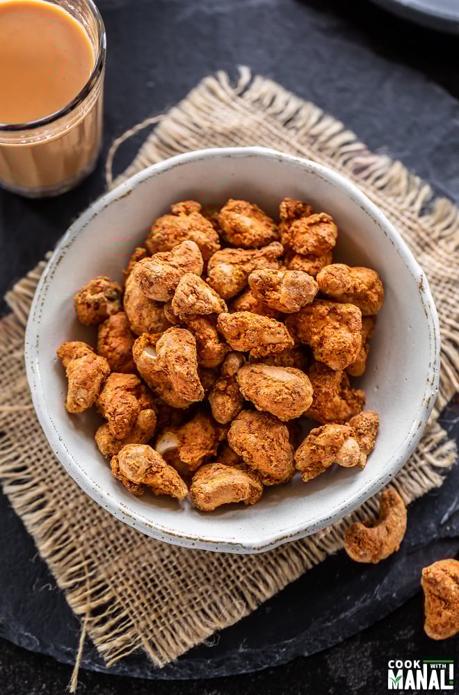 spicy cashews placed in a bowl with a glass of chai on the side