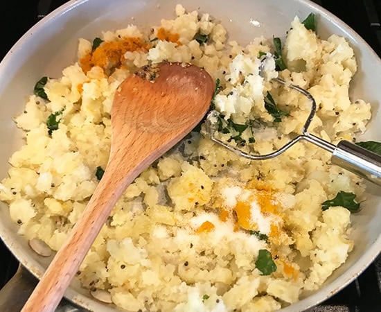 mashed potatoes being stirred with spices using a wooden spatula