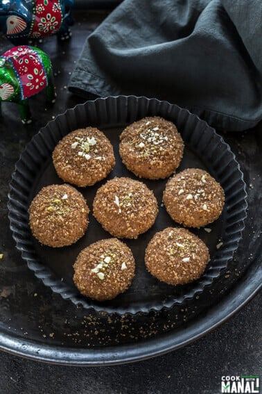 seven pieces of mathura peda in a black rimmed plate with a grey color kitchen towel on the side