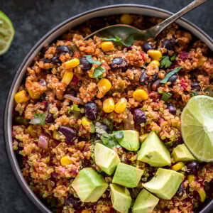 mexican quinoa in a round black bowl, garnished with diced avocados and a lime wedge