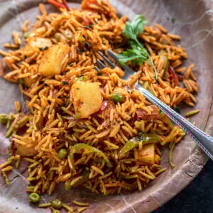 rice with vegetables like potato, pepper garnished with cilantro served in a paper plate