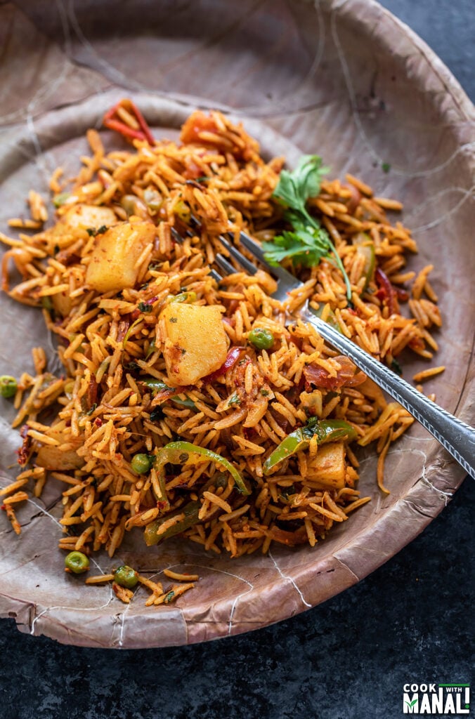 rice with vegetables like potato, pepper garnished with cilantro served in a paper plate